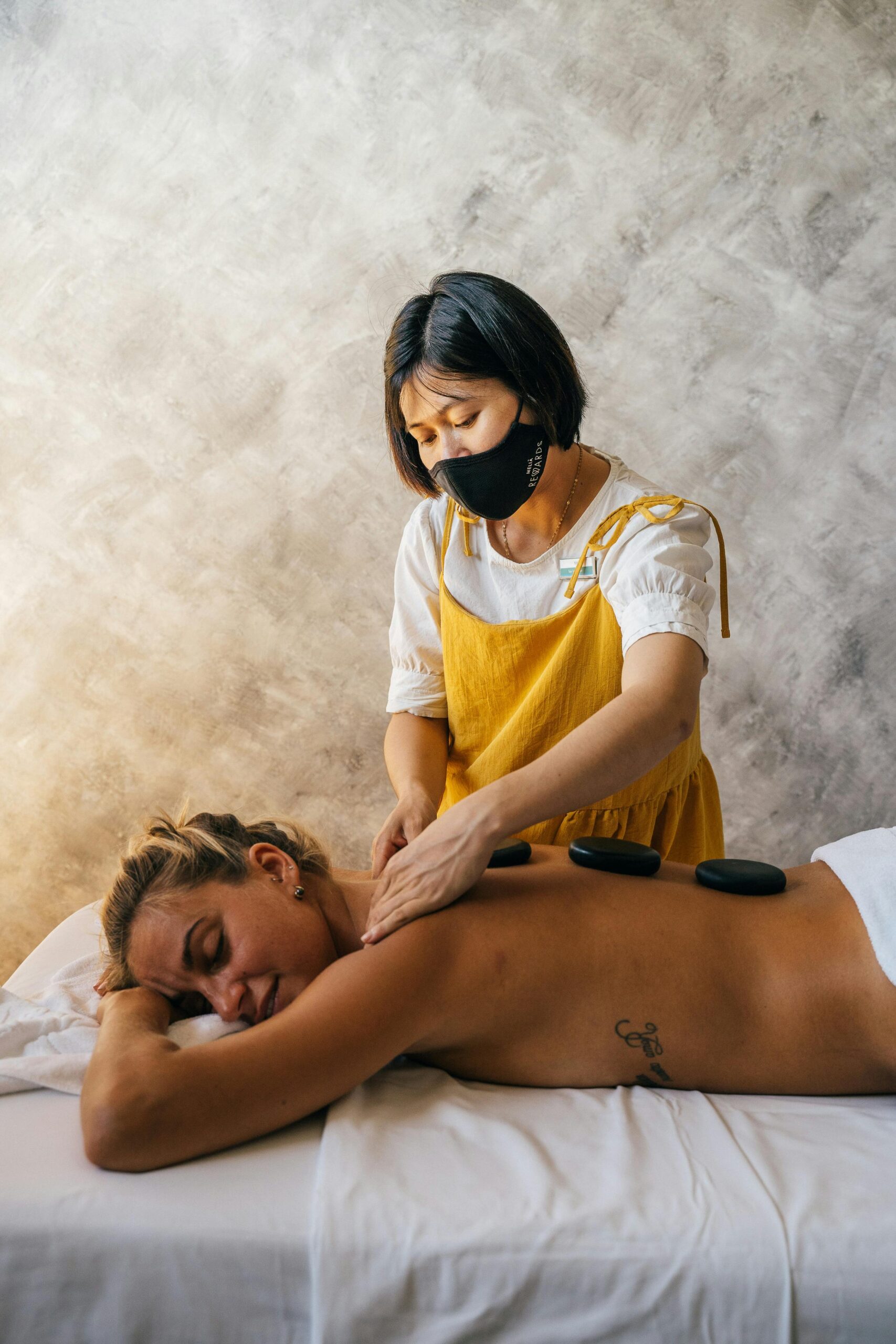 A therapist providing a relaxing hot stone massage to a woman in a serene setting, promoting wellness.